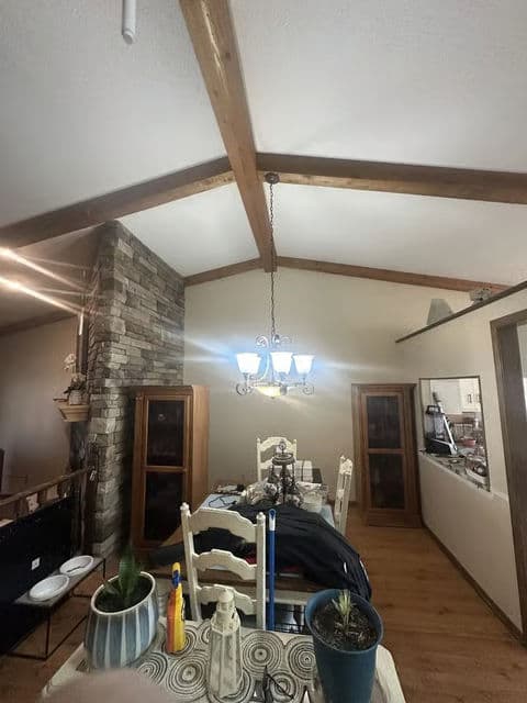 Dining area with a wooden beam ceiling, chandelier, and stone wall accents.