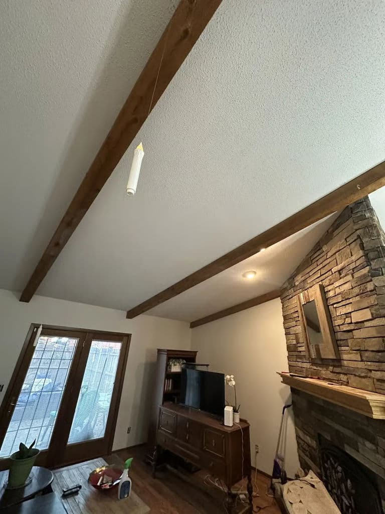 Living room with wooden beams, stone fireplace, and large windows for natural light.